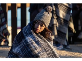 2022 年 12 月 22 日，一名哥伦比亚移民在得克萨斯州埃尔帕索的美墨边境围栏旁露营过夜后，裹着衣服抵御寒冷。