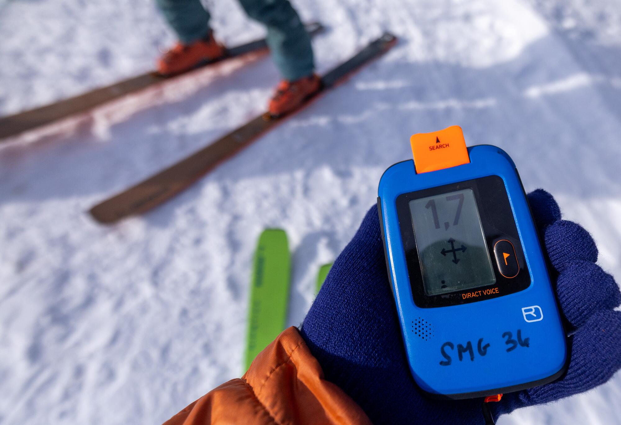 A skier holds an avalanche rescue beacon in a mittened hand.